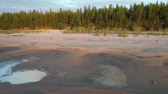 The drone flies away from a deserted sandy beach with a forest