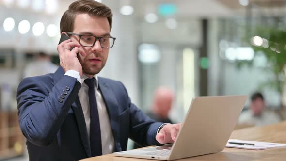 Businessman with Laptop Talking on Smartphone at Work 