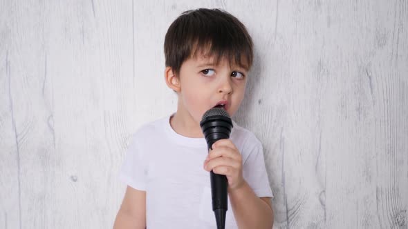 Boy in a White t Shirt Stands Against a White Wall and Sings Karaoke