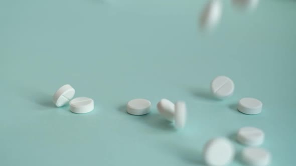 White Pills Falling on Blue Background in Slow Motion