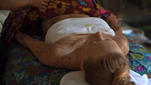 Closeup Shot of a Young Woman in a Tropical Spa. Beautician Applies Body Skin Scrub