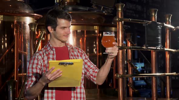 Young Man with Clipboard Working at Craft Brewery, Examining Beer