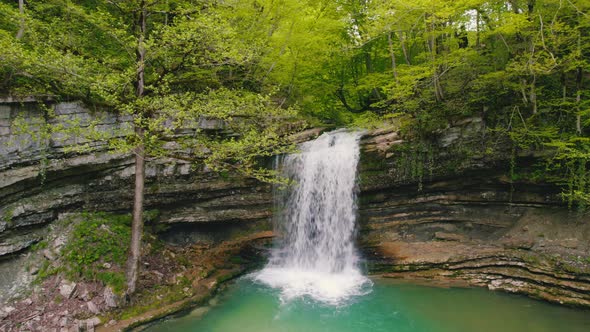 Stunning Scenery of a Small Waterfall and a Green Lake in the Forest Scenic Drone Shot