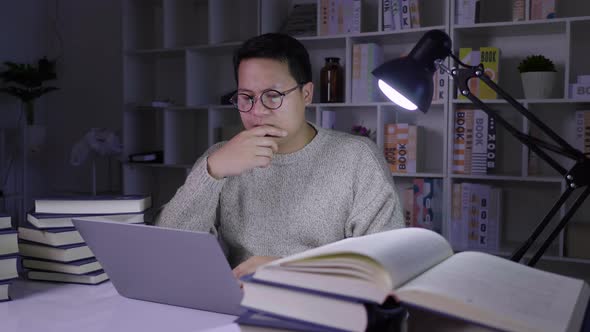 Serious man working on laptop at night, determining information with stressed face on working table