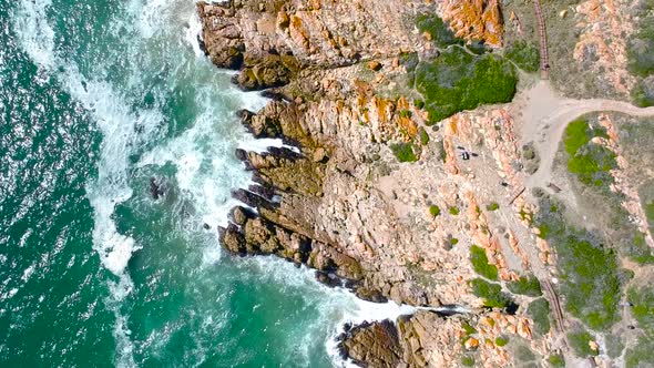 Top Down View of rocky coastline with turqoise waves crashing into the rocks on a sunny day