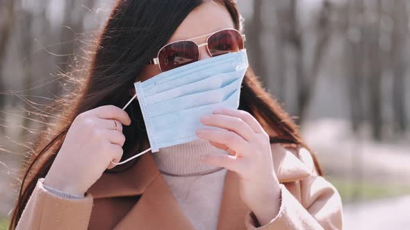 Woman in a Coat Is Putting a Protective Mask on Outside