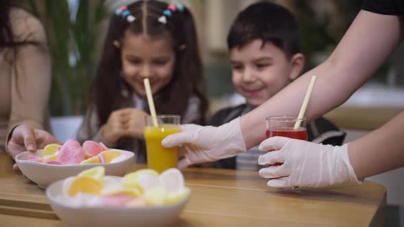 Waitress Hands Serving Yellow and Red Juices for Cheerful Middle Eastern Boy and Girl Sitting at