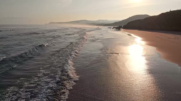 Northern Spain, Morning Beach During Sunrise. Waves Rolling on Coast, Bright Sun Reflecting on Wet