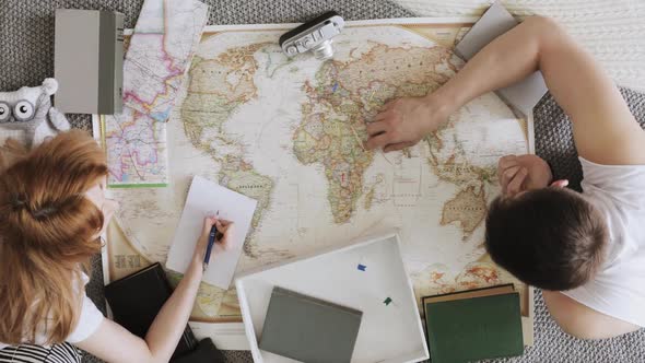 Man and Woman Planning Vacation Using a World Map and Other Travel Accessories