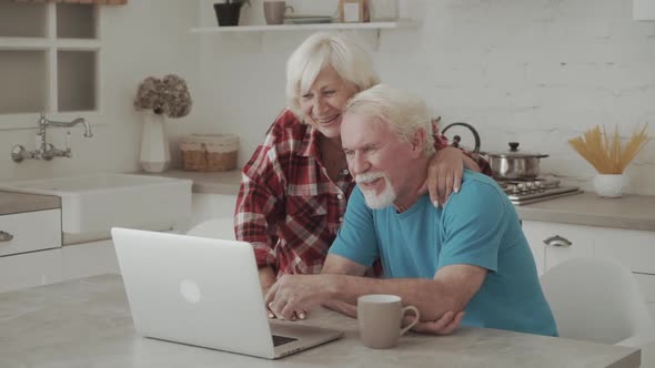 Happy Senior Couple Looking at Laptop Laughing Watching Comedy Movie Making Distance Video Call