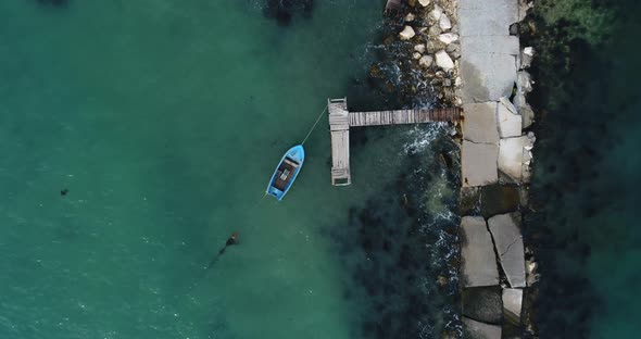 Aerial video of lonely fishing boat and wooden pier in turquoise ocean, sea. Top view