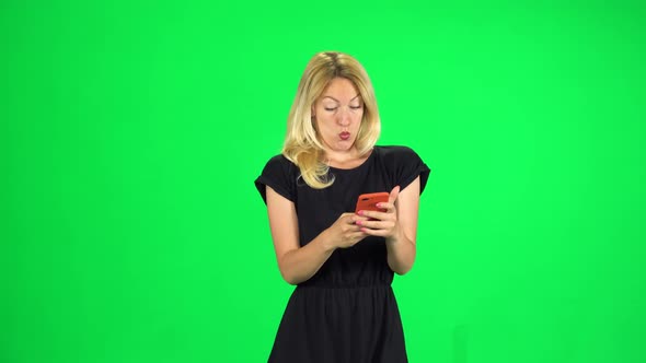 Smiling Woman Goes and Texting with Smartphone on Green Screen at Studio.