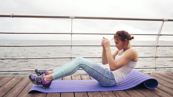 Young Athletic Woman Doing Situps on the Mat By the Ocean in the Early Morning