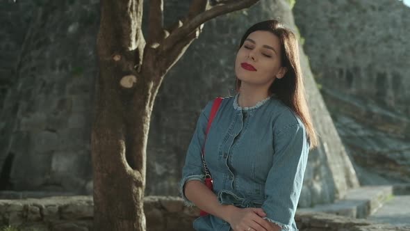 Young smiling brunette woman with red lipstick in denim overalls  sits on sunlights