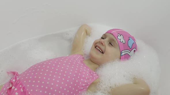 Cute Blonde Girl Takes a Bath in Swimwear. Little Child Washes Her Head