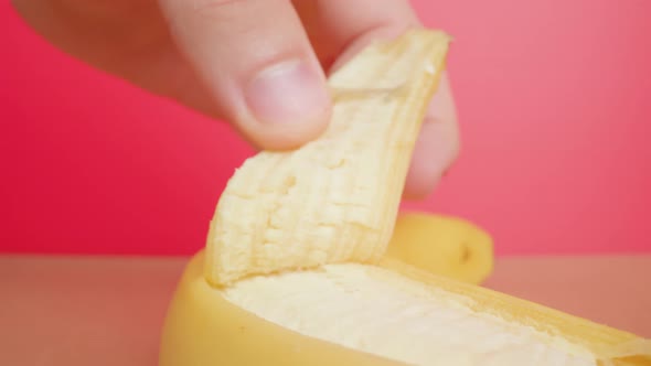 Person Peels Yellow Banana Skin on Pink Wall Background