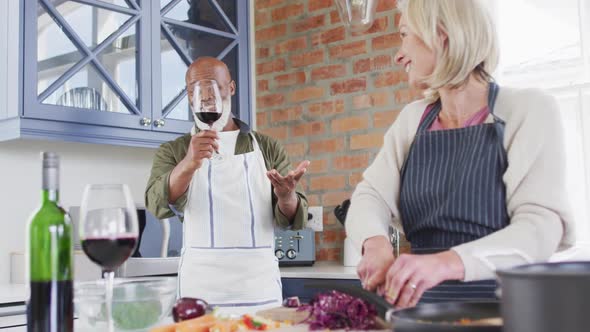 Mixed race senior couple wearing aprons talking while cooking together in the kitchen at home