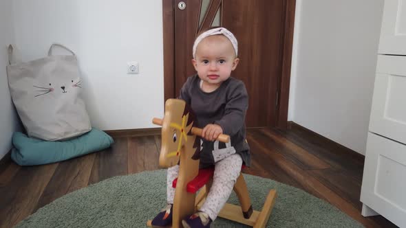 Happy baby girl playing on wooden rocking horse. Childhood, game at home concept alt