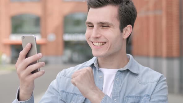 Outdoor Young Man Celebrating Success on Smartphone