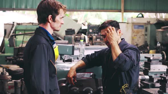 Tired Factory Workers Taking a Break and Talking to Coworker in the Factory