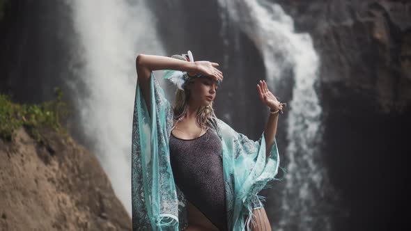 Adorable and Flexible Female Dancer Posing in Movement on a Cliff Before the Waterfall