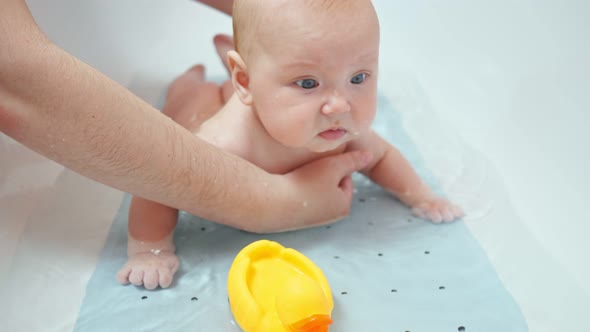 Interested Baby Girl Plays with Father and Toy Duck in Water