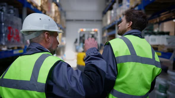 Live Camera Follows Experienced Senior and Young Caucasian Man Walking in Warehouse to Forklift