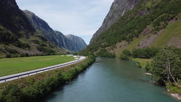 European road E39 passing through deep valley between glacial river and green farmland grass fields