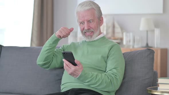 Old Man Celebrating Success on Smartphone at Home