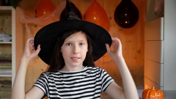 Teen Girl in Witch Costume and Black Hat Puts on Protective Face Mask to Celebration Halloween