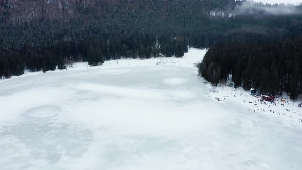 People on banks of frozen Saint Ann (Sfanta Ana) volcanic crater lake, Romania. Aerial forward