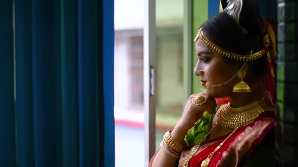 Newly wed Romantic and beautiful Indian bride looks outside through window on rainy evening