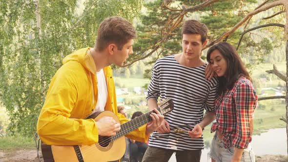 Young Cheerful Couple Enjoying Listening To Their Friend's Playing the Guitar