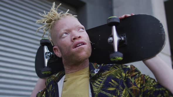 Happy albino african american man with dreadlocks walking and holding skateboard