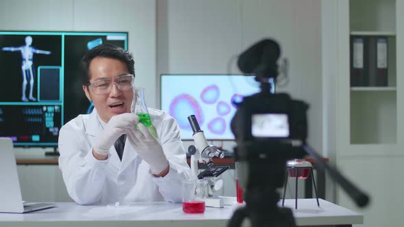 Young Asian Male Research Scientist Holding Glass Test Tube And Speaking To The Camera alt