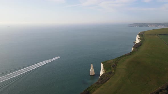 Motorboat navigating along coast of Old Harry Rocks cliffs leaving long white wake, England. Aerial