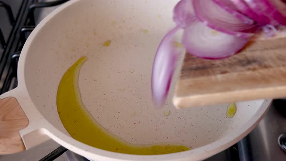 Put sliced raw purple onions in white frying pan with heated olive oil close up