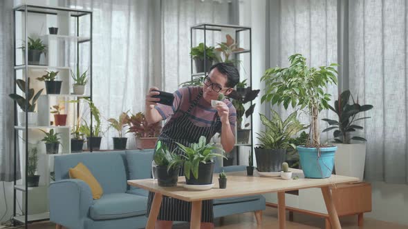 Asian Man Holding Plant And Taking Photo By Smartphone At Home
