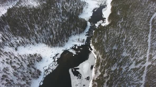 Flight over a frozen river and winter snowy forest