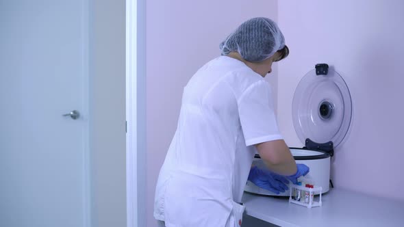 Woman Lab Technician in a White Coat Comes to a Centrifuge