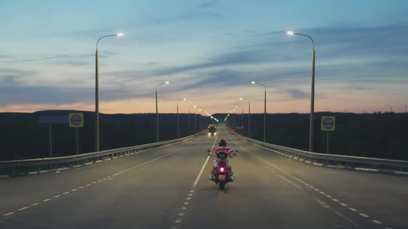 Biker in helmet with an American flag wrapped around his neck rides along the highway