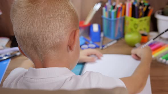 Closeup of a Small Schoolboy Writing in a Notebook Sitting at the Table at Home