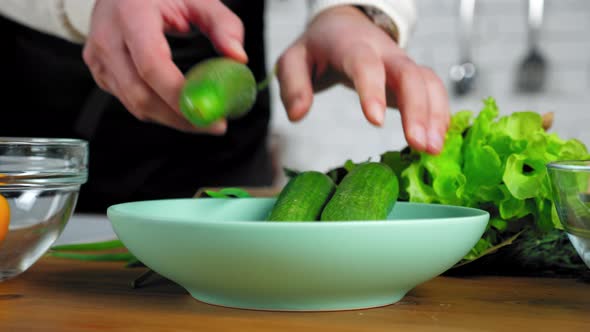 Close up chef man hands put fresh food cucumbers in plate at home kitchen
