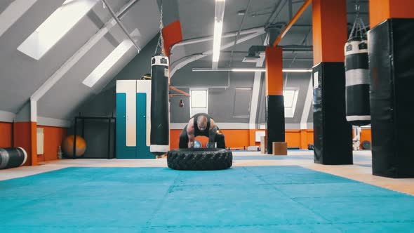 A Man Bodybuilder Flips a Tire on the Floor Over and Over