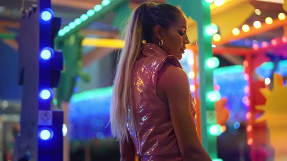 Woman In Pvc Clubwear Posing Amongst Neon Fairground Lights