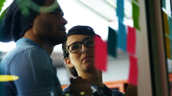 Executives discussing over sticky notes on glass wall