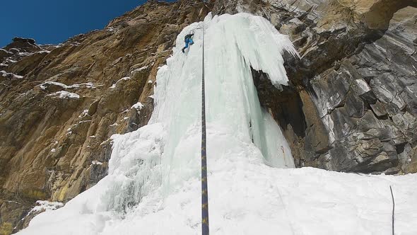 Man Climbing Ice Waterfall with Rope and Ice Axe