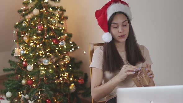 Young Brunette Female Student in Red Santa Hat Streaming Laptop Showing Gift Box