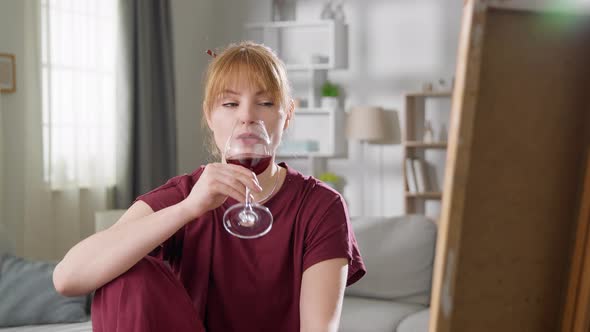 Beautiful Woman Artist Draws a Picture of the House and Drinks Red Wine From the Glass