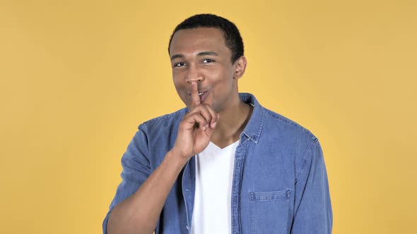 Young African Man Gesturing Silence Finger on Lips Yellow Background